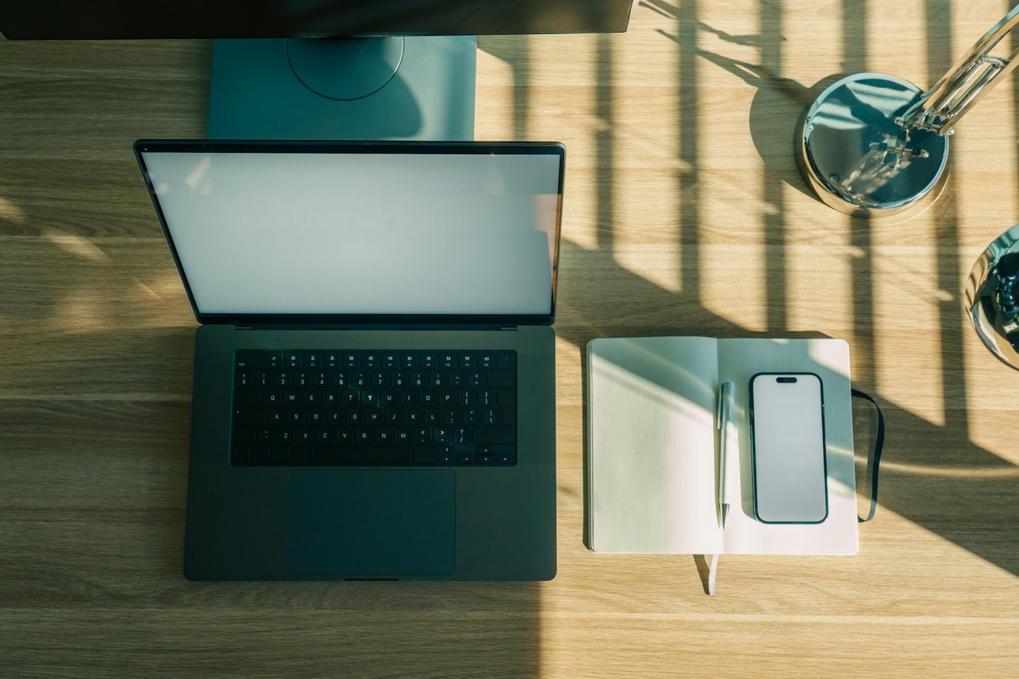 Ordinateur portable, carnet et smartphone disposés sur un bureau en bois.